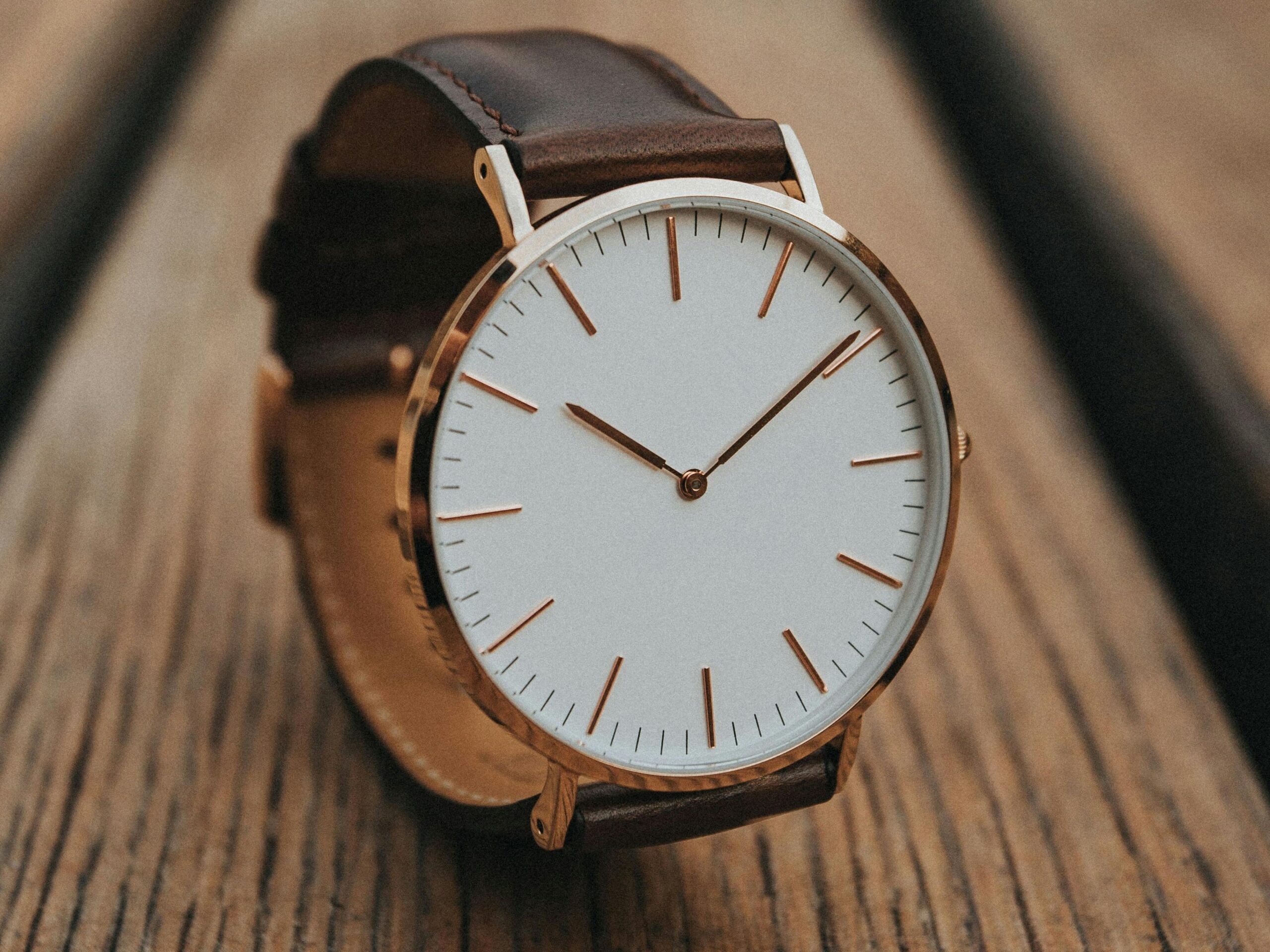 Close-up of a minimalist analog watch with brown leather strap on a wooden surface.